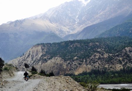<h3>Riding into Muktinath Valley</h3>
From the moment we leave Jomsom, it feels as if we have entered a new world. Now in the subalpine zone (3,000meters +), the peaks of the Dhaulagiri and Nilgiri mountains soar above us. The landscape is rocky and barren with a sharp contrast between the light brownish hue of the terrain and the ethereal vivid blue of the sky. We ride along a stony serpentine road that writhes its way ever deeper and higher into Muktinath valley (3,700meters). Up ahead on the left, we see a village with small green terraced fields. We turn right, on the road that continues climbing towards Jharkot. The Royal Enfield is adept at riding such roads and the sensation of being on the roof of the world is indescribable. 